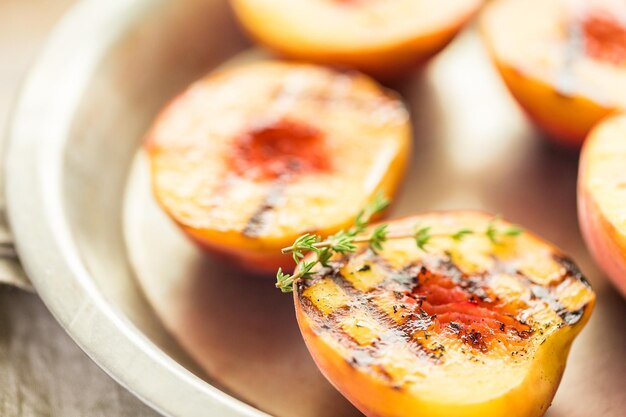 Organic grilled peaches with fresh thyme on a metal plate.