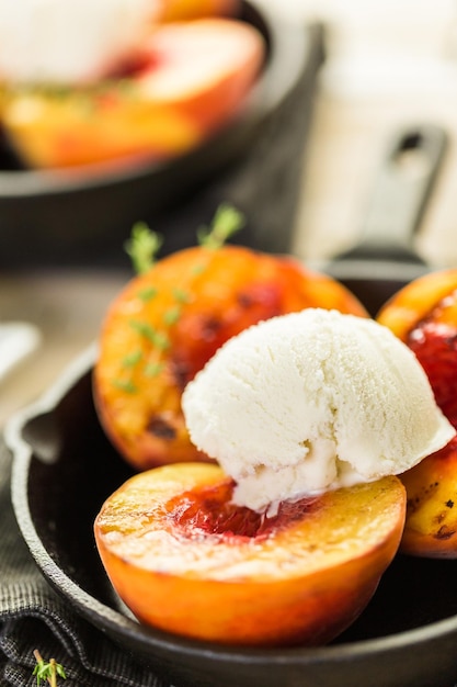 Organic grilled peaches with scoop of vanilla ice cream on a cast iron frying pan.