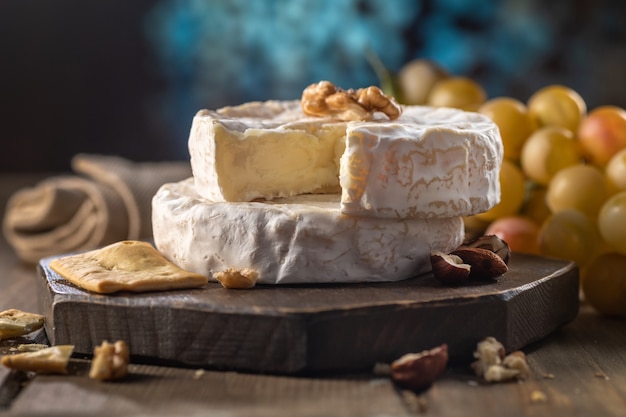 Фото Органический домашний камамбер или сыр бри на деревянной доске с виноградом, орехами и медом. деревенский стиль.