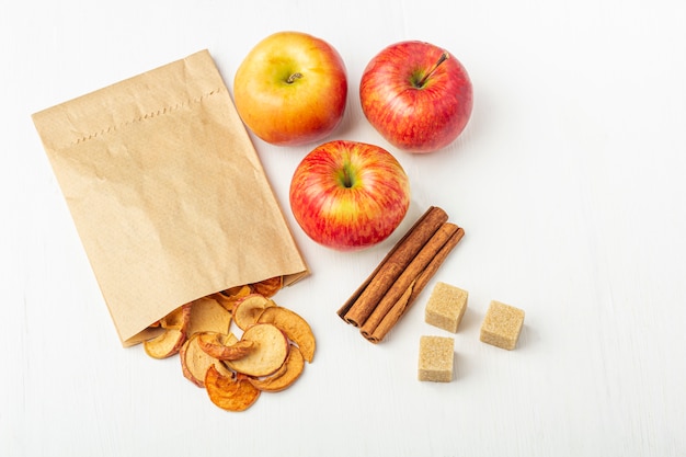 Organic homemade dry fruit chips in a paper eco pack and apples, cinnamon sticks, cane sugar on white