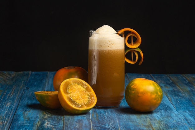 Photo organic lulo or naranjilla south america exotic fruit. slice and whole fruits and juice glass on old blue table and dark background. solanum quitoense, dark food