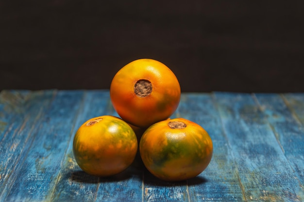 Frutta esotica biologica lulo o naranjilla sud america. frutto intero su legno blu e sfondo scuro. solanum quitoense, cibo scuro