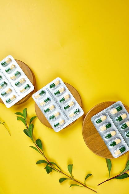 Organic medical pills, capsules in blisters with herbal plant on a yellow surface