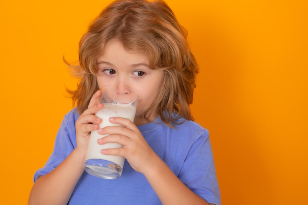 Organic milk Beautiful smiling child with a glass of milk Cute boy in blue shirt holding glass of milk on yellow isolated studio background Portrait of funny kid with milk mustache