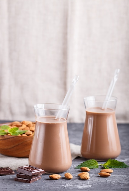 Organic non dairy almond chocolate milk in glass and wooden plate with almond nuts on a black concrete background.