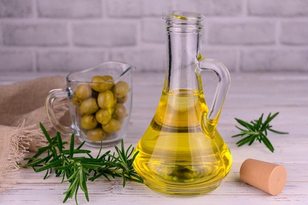 Organic olive oil in a glass bottle and green olives with rosemary on a wooden background.