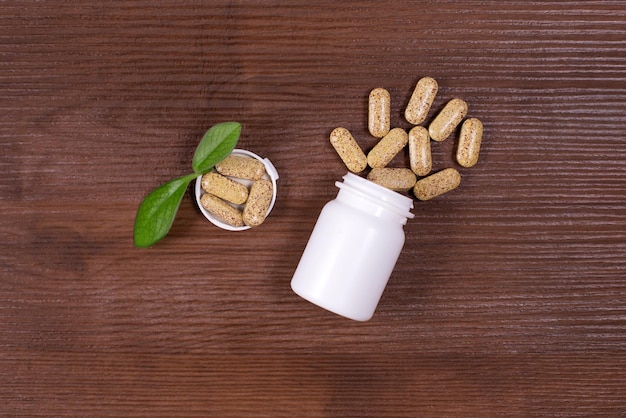 Organic pills on green leaf and jar on wooden background