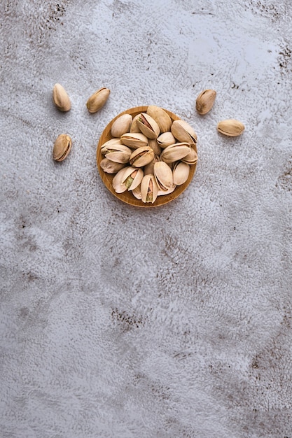 Organic pistachio nuts in wooden bowl on gray table. Top view, Space for text