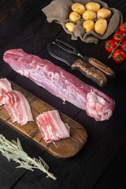 Organic pork fillet with ingredients and herbs for grill or baking, sage, potatoe set, on black wooden table