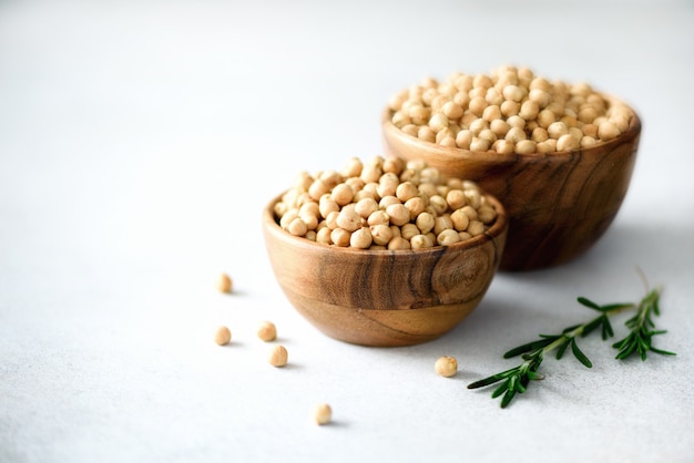 Organic raw chickpeas in wooden bowls and rosemary on gray concrete. Healthy food ingredients. Copy space.