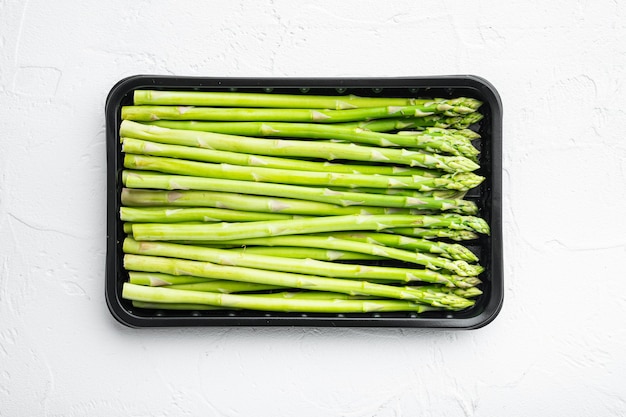 Organic raw ripe green asparagus set, in plastic market container, on white stone