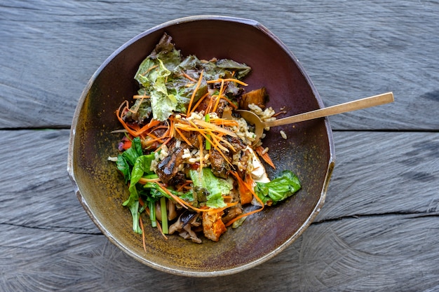 Organic salad from green curry rice, eggplant, kimchi, braised greens, mushroom, tempeh bacon, tofu is served in a clay bowl. Close up. The concept of healthy eating.