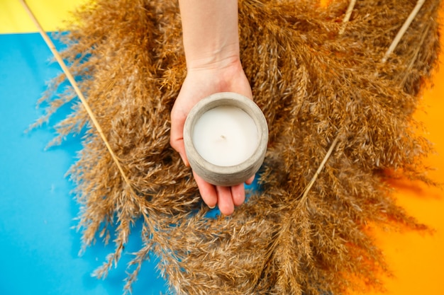 Organic scented candle in a glass with gray concrete cement. Loft interior, minimalism concept. Close up, copy space for text. Around dry clumps of branches