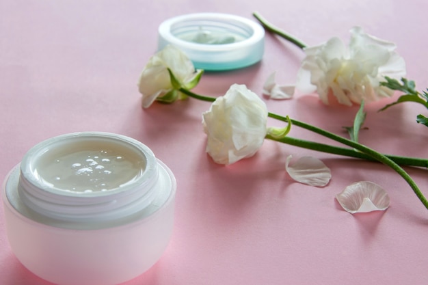 Organic skin care product and delicate flowers on pink background. Healthy cosmetic products . Wellness beauty treatment.