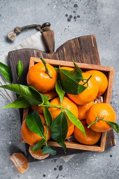 Organic Tangerines, mandarins with green leaves in wooden box. Gray background. Top view.