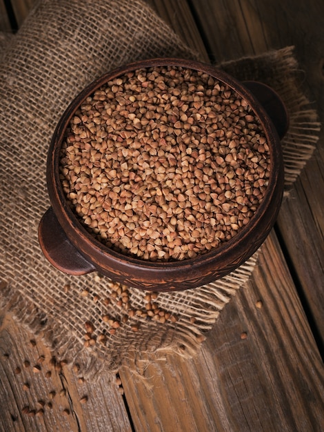 Organic uncooked scattered buckwheat grain in a bowl on a rustic wooden background. Healthy and diet food concept.