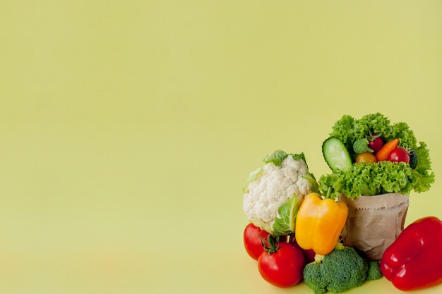 Organic vegetables broccoli cucumbers bell peppers apples in brown paper Kraft grocery bag on yellow background. Healthy diet dietary fiber vegan plastic free concept. Poster banner