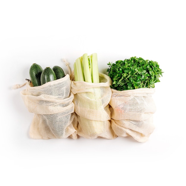 organic vegetables and fresh greens in reusable produce bags on white background