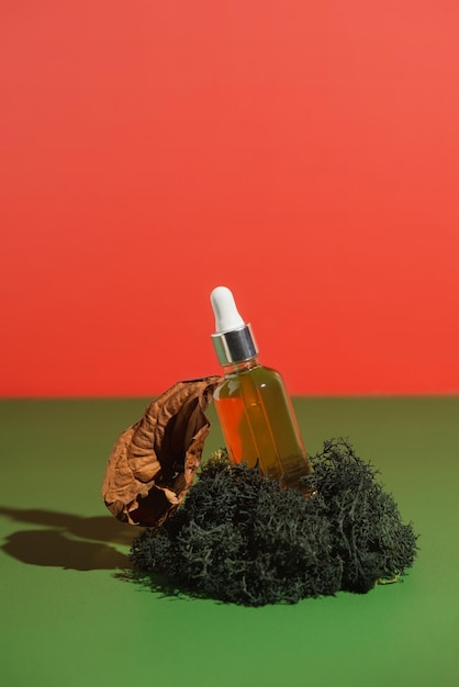 Organic vitamin serum in transparent bottle on green moss with dry flower selective focus