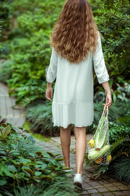 Organic. Woman in white dress going and carrying bags with different vegetables