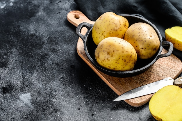 Organic yellow potatoes in a pan. Black background. Top view. Copy space