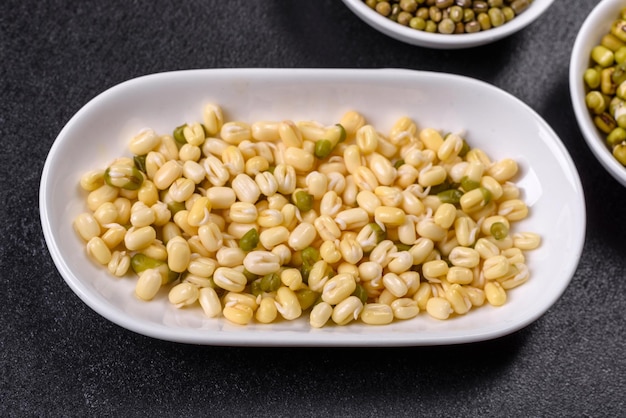 Organics fresh baby green bean sprouts in white ceramic bowl on\
a dark concrete background