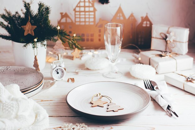 Organisatie van een feestelijke kersttafel. Bord, bestek, champagneglas en kerstversiering. Tablescapes op witte houten tafel