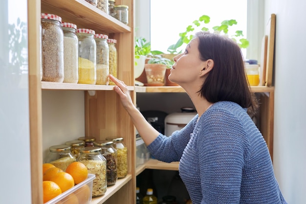 Organisatie van pantryvrouw in keuken dichtbij houten rek met blikken en containers van voedsel