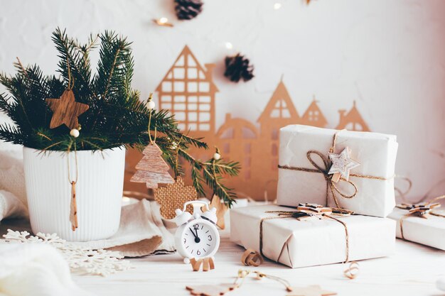 Organization of a festive Christmas table. Gifts in craft paper, an alarm clock and a fir bouquet in a vase on the Christmas table. Eco-friendly and homemade lifestyle