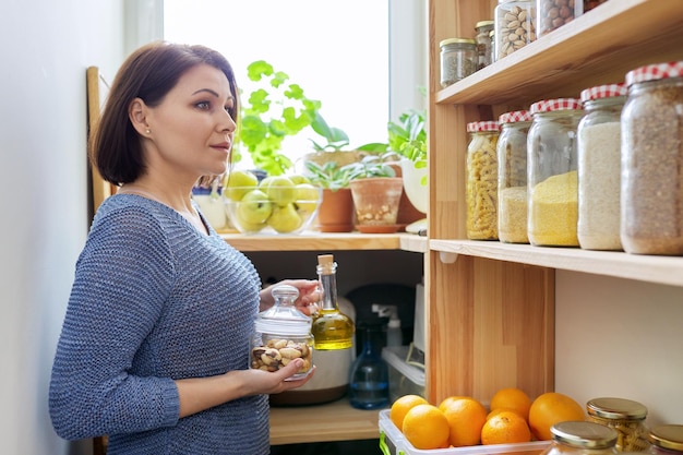 Organization of pantry woman in kitchen near wooden rack with cans and containers of food