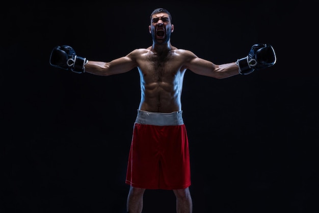 Oriental boxer celebrating his victory with raised arms in black gloves