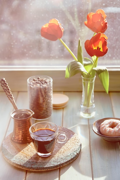 Oriental coffee in traditional turkish copper coffee pot with
flowers on window sill wooden windowsill with orange tulips and
hyacinth flower pot rainy day in spring cozy scene hygge
concept