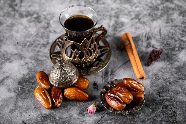 Oriental dates on an ethnic style saucer with a glass of tea and cinnamon sticks. top view