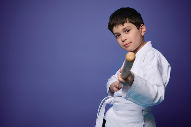 Oriental martial arts practice Aikido wrestler in white kimono with wooden weapon bokken practices fighting skills on purple background copy ad space