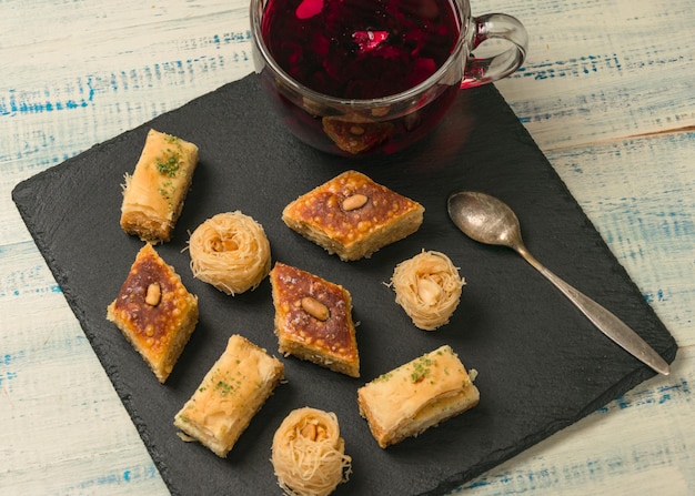 Oriental sweets and red fruit tea on a black stone on a wooden background