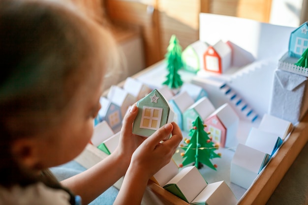 Origami adventskalender. Leuk meisje dat naar kleine papieren huizen kijkt, seizoensgebonden activiteit met kinderen