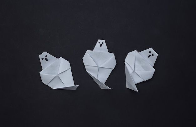 Origami ghosts on black background. Handmade halloween decor. Top view