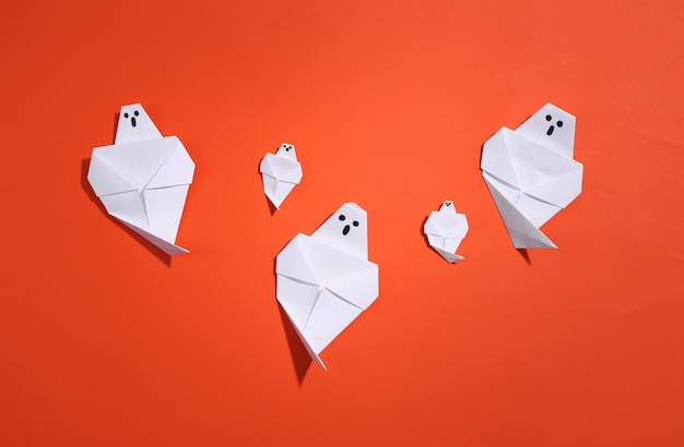 Origami ghosts on orange bright background. Handmade halloween decor. Top view