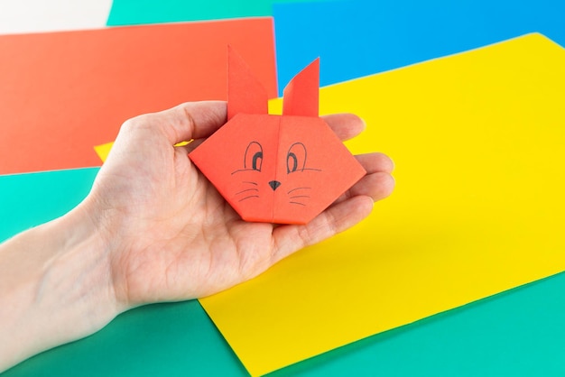 Origami paper rabbit in hand on a background of multicolored paper