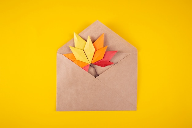 Origami papercraft autumn concept fallen leaves letter in an envelope on a yellow background handmade craft art