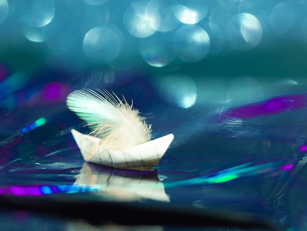 Origami ship sailing on the waves of the sea, made of colored shiny paper with bokeh.