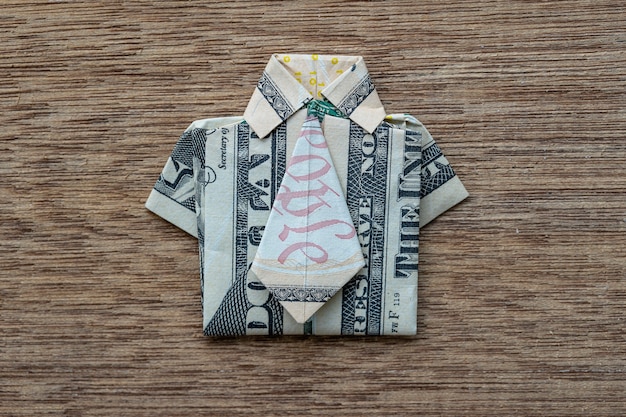 木製の背景にドル紙幣で作られた折り紙シャツ。閉じる。ドル紙幣Tシャツ