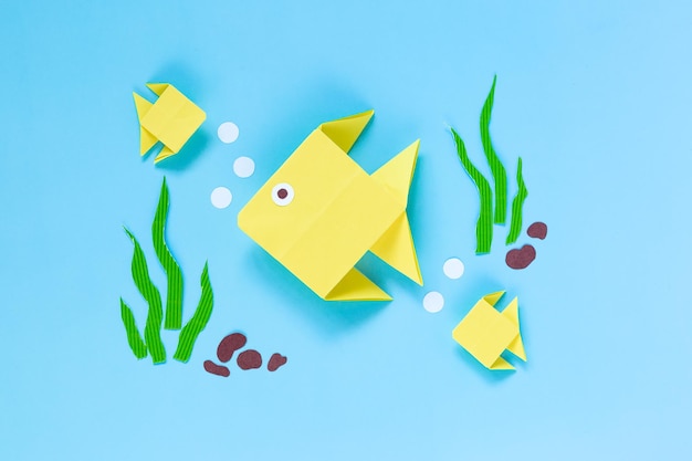 Photo origami yellow fish on a blue background. children's craft