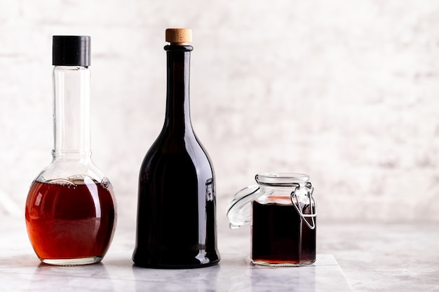 Original glass bottles with different vinegar on a marble table against a table of a white brick wall. Copy space. Horizontal.