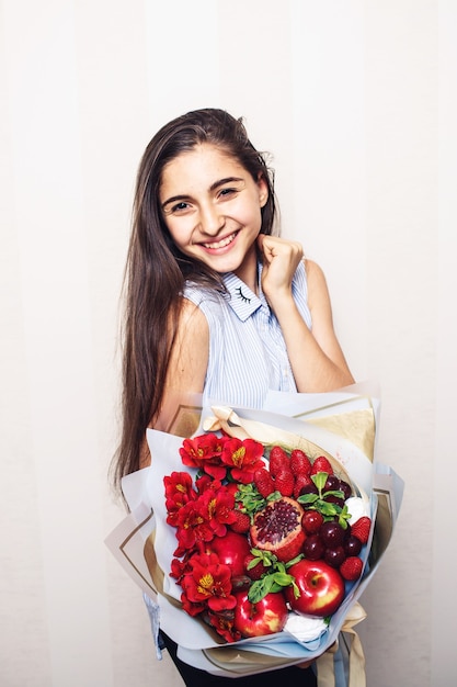 Original unusual edible bouquet of fruits in the hands of a girl on a light background.