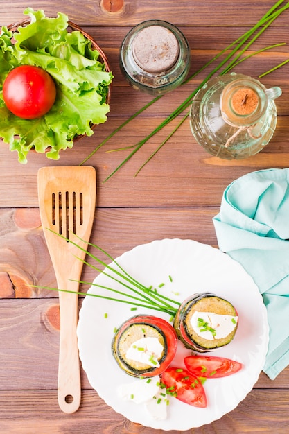 Origineel voorgerecht van gebakken courgette, verse tomaten en feta-kaas op een houten spies op een witte plaat. Houten tafel. Bovenaanzicht