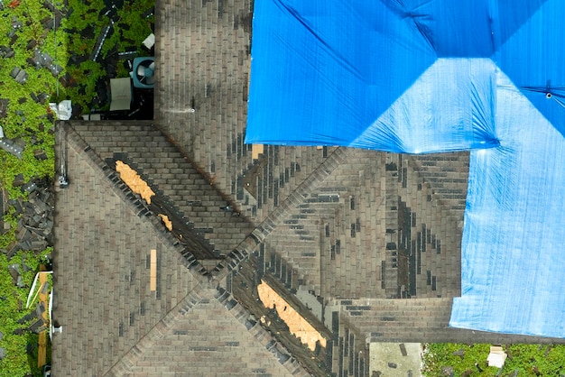 Orkaan Ian beschadigde dak van huis bedekt met beschermend plastic zeil tegen regenwater dat lekt tot vervanging van asfaltshingles Na een natuurramp