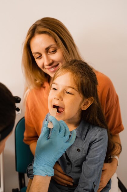 Procedura di orofaringoscopia per bambino l'otorinolaringoiatra esamina la gola del bambino con la spatola consultazione familiare con il laringologo