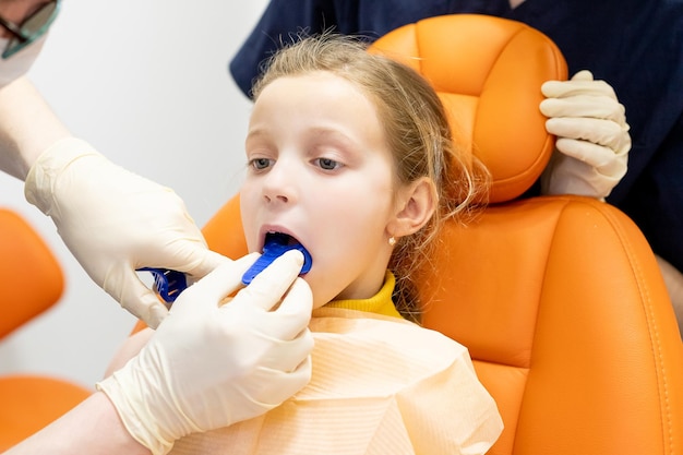 The orthodontist demonstrates to the girl patient the impression tray in which the silicone impression material will be placed to get the shape of her teethChild during orthodontist visit