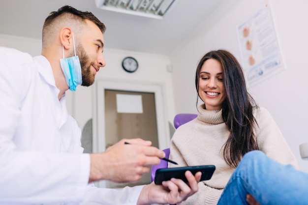 Orthodontist houdt telefoon vast met röntgenfoto van kaak en laat deze aan vrouwelijke patiënt zien. orthopantomogram.